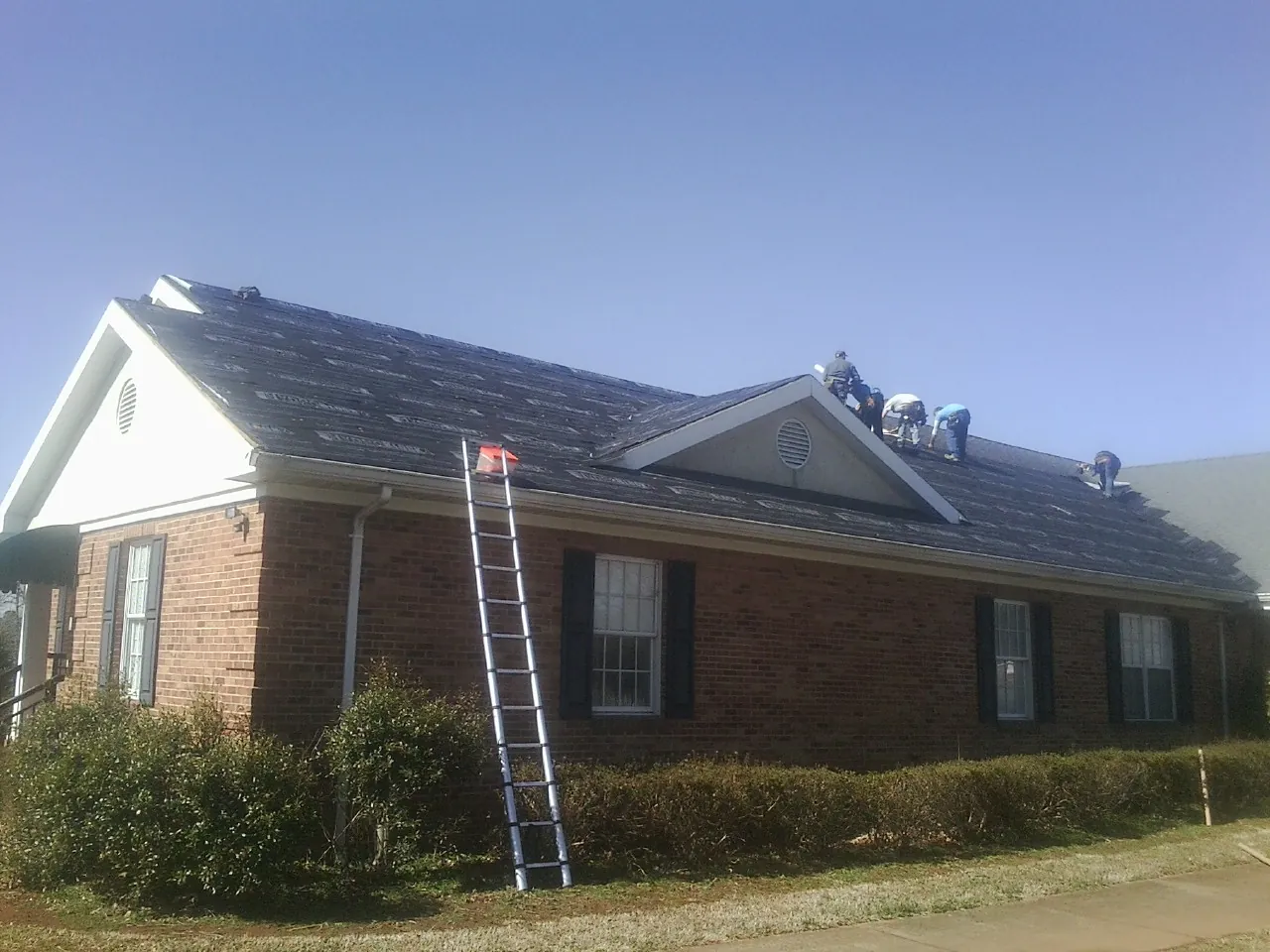 Crew tearing shingles off a brick ranch roof with a ladder set — Metal Roof Repair work by our crew in Alloway