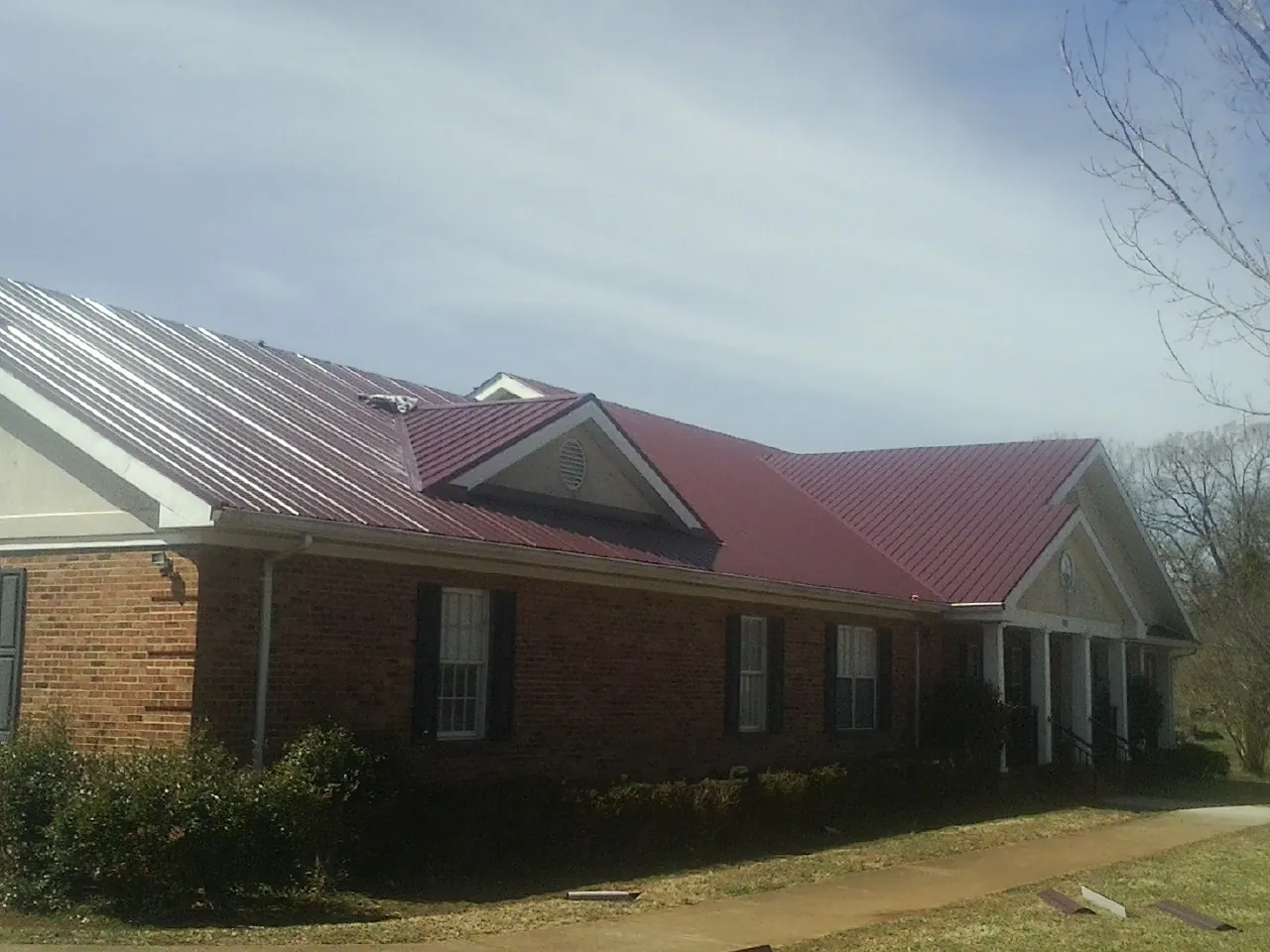 Red metal roof with gabled entries on a long brick building, from a Hail Damage Roof Repair job in Alloway