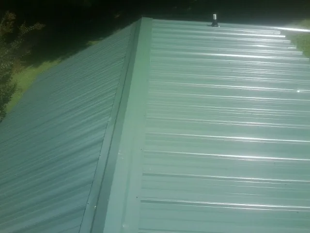 New green metal panels meeting at the ridge of a roof — Flat Roof Repair work by our crew in Alloway