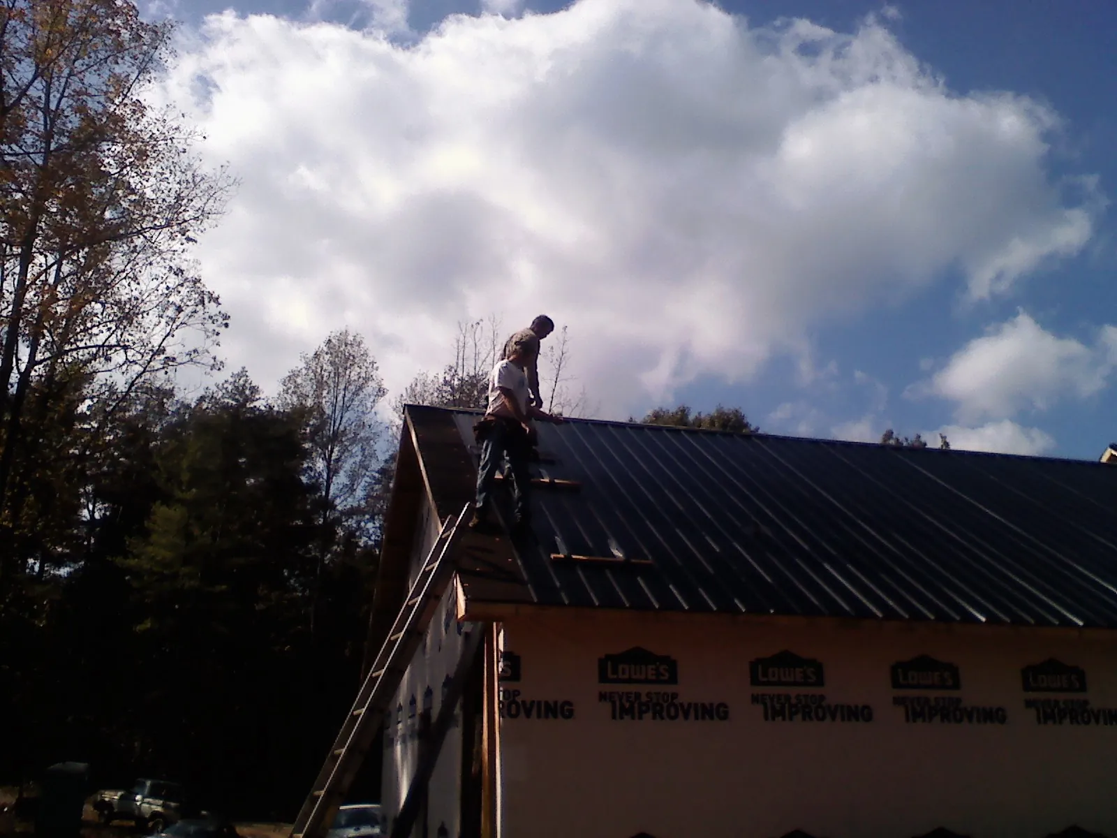 Roofer fastening dark metal panels high against a cloudy sky, from a Roof Inspection job in Alloway