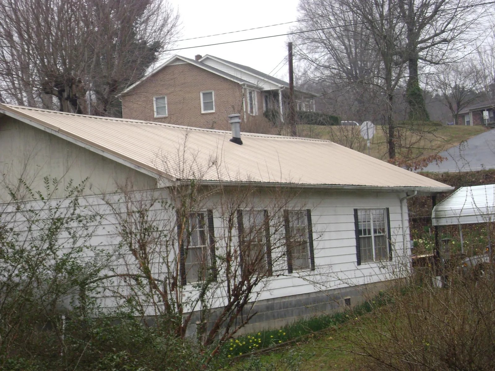 Tan metal roof on a white sided house set into a hillside — Commercial Roofing by Roofing Brothers in Alloway